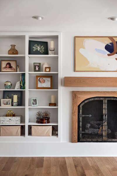Living room renovation with open built-in shelves, wood fireplace trim, decorative accessories, and light wood floors.