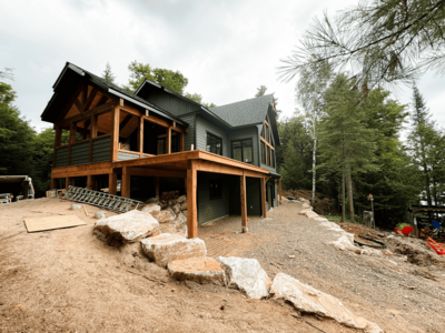 Handcrafted timber frame house under construction in Haliburton Highlands, surrounded by scenic forested landscape.