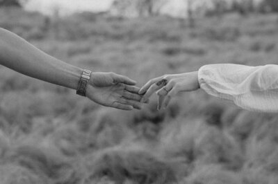 A black and white photo of 2 hands reaching towards one another in a romantic, longingly way.