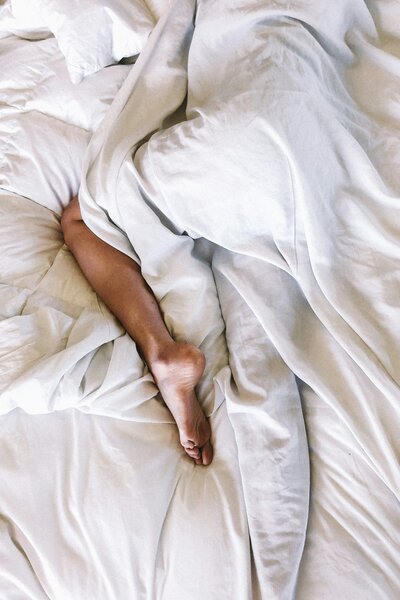 Bare legs on white sheets symbolizing intimacy and wellness—sexual regeneration support through hormone balancing and personalized therapies
