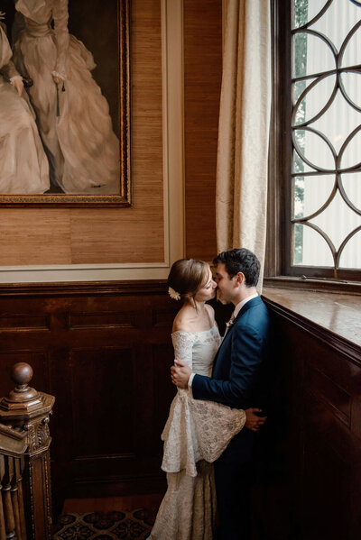 couple kissing in warm wooden estate room. groom in blue suite.