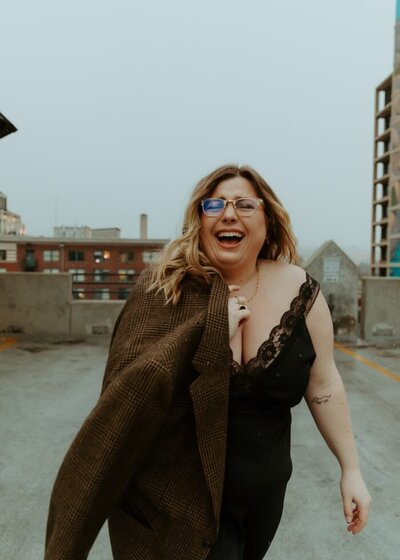 Wedding Photographer Maggie of Maggie Grace Photo stands on a building rooftop and smiles at the camera.