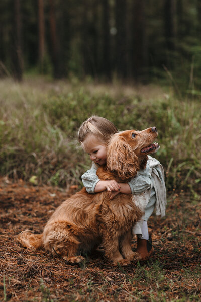 Child and dog hug in the woods