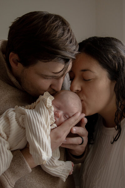 New parents kissing their newborn baby girl during an in-home newborn lifestyle session