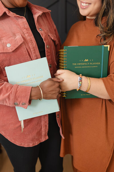 two women hold paper planners and smile