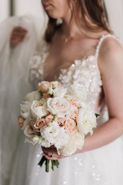 Bruid in trouwjurk met bruidsboeket, begeleid door weddingplanner op haar grote dag.