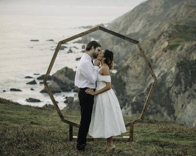 husband and wife in front of geometrical arch on the coast