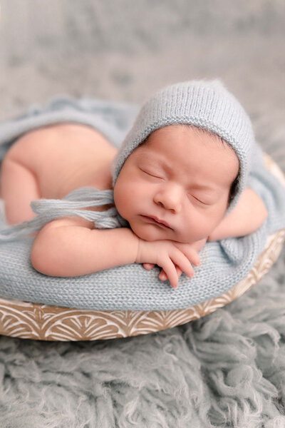 baby boy wearing blue bonnet in blue bucket sleeping