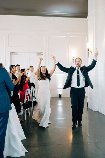 Bride and groom enter their reception hand in hand as their guests cheer. Photo by Anna Brace, who specializes in NE Wedding Photography.