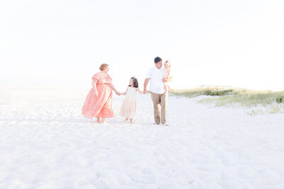 A family of four holding hands and walking on the beach during sunset at St. Andrews State Park.