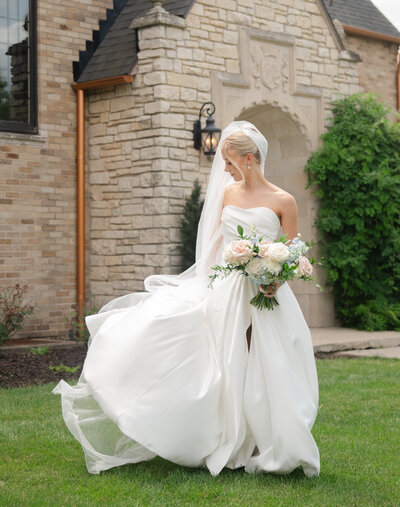 A bride twirls in her dress in front of a old stone manor in Grand Rapids