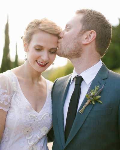 Bride looking down smiling as Groom kisses her left temple