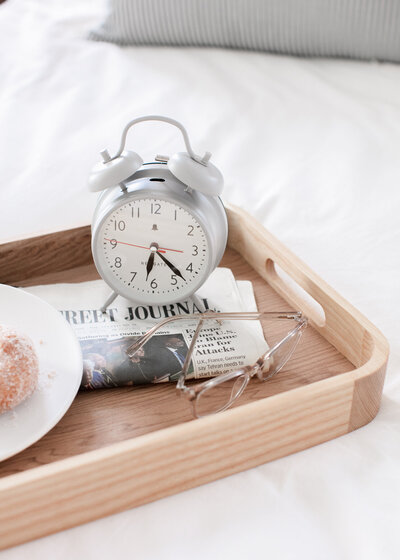 tray with old fashioned alarm clock, reading glasses, and newspaper, and plate with a pastry.