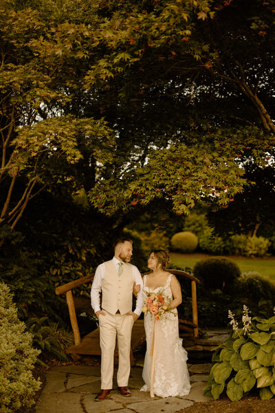 Bride and groom surrounded by greenery and a wooden bridge with a colorful bouquet