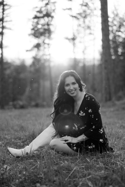 Black and white photo of Aurelia from Aurelia K Photography, sitting in a field smiling and looking at the camera.	