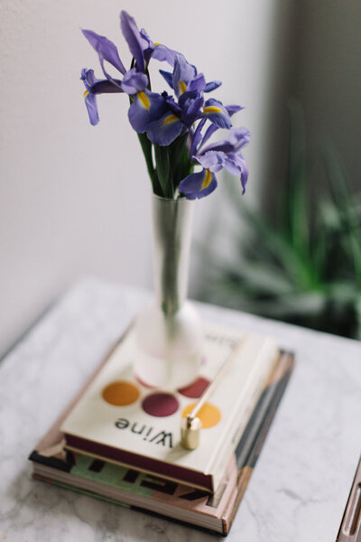 Stack of colorful books under a vase of purple flowers