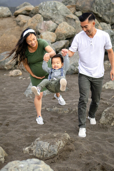 Candid moment of mother and father swinging son at the beach by Bay Area family photographer
