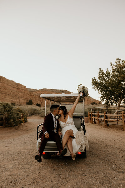 bride and groom kissing on the back of a golf cart in the desert