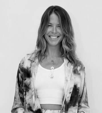Black and white photo of woman with long, curly hair wearing a crop top and tie-dye kimono smiles at camera.