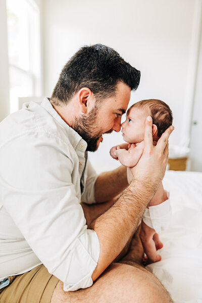 Light bright photo of father touching noses and smiling with newborn baby in thier home near st. petersburg