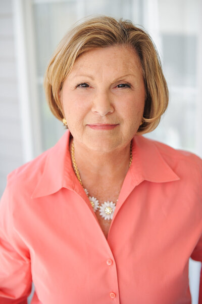 Headshot of Devon Gedney, President of PEO North Carolina chapter 2024, wearing a peach shirt and flower necklace.