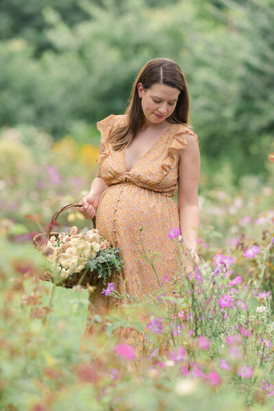 A new mother wearing an orange dress picks flowers  in a botanical garden.