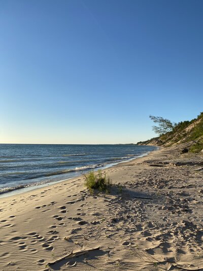 Lake Michigan beach with footprints in the sand and waves rolling up on shore.