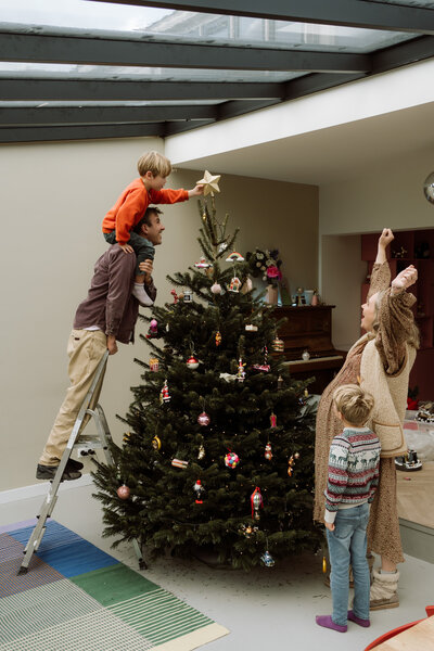Gezinsmoment van de piek op de kerstboom zetten tijdens een lifestyle shoot.