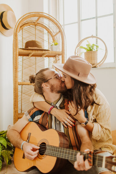 Couple playing guitar kissing in boho living room space