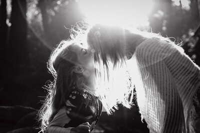 black and white image of young sibling kissing her old sister on the forehead.