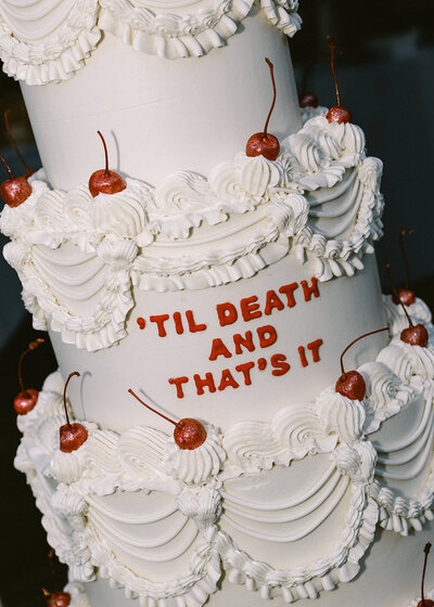 traditional tiered wedding cake that reads "til death and that's it"