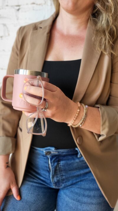 Close-up of Julie Wenzlick holding pink coffee mug and glasses, offering retainer support for small business owners
