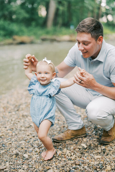 dad helping little girl walk near the creek