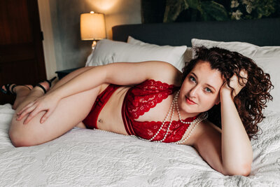 Boudoir photo Missoula woman laying on bed wearing red lingerie and pearls