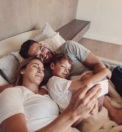 A family smiles with their eyes closed as they cuddle together on the same bed. This could represent a couple finding common ground with the love of their child after affair counseling in Florida. We offer affair recovery counseling and other services. Contact an affair recovery therapist for support in healing from infidelity today