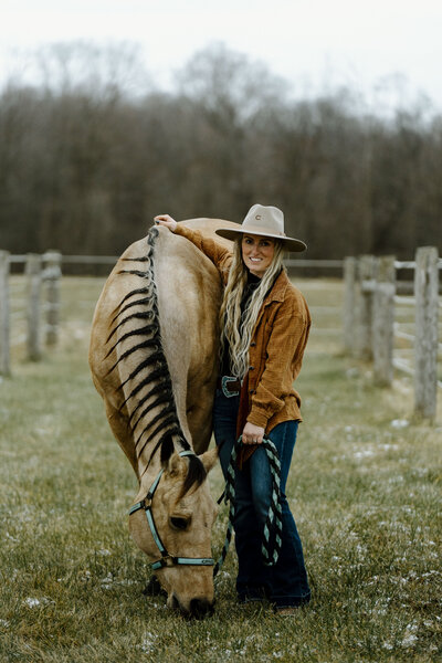 a girl standing next to her buckskin horse