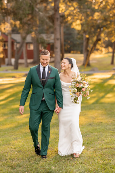 Bride and groom holding hands and walking outside in the sunlight