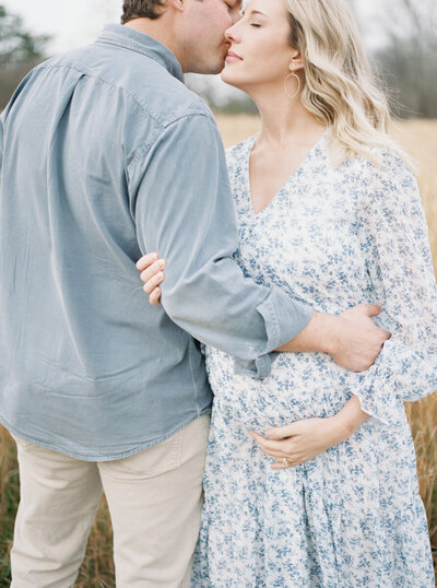 A couple embraces during their maternity shoot in a grassy field by Huntsville photographer Kelsey Dawn Photography
