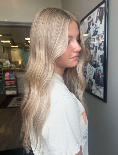 A young woman with long, platinum blonde hair styled in soft waves, showcasing a radiant hairstyle created by 212 Salon, Spa, & Barbershop.