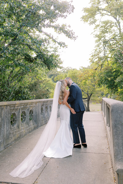 A couple kisses walking across a stone bridge at Eden Park.