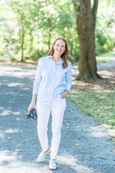 photographer holding a camera outside wearing white jeans
