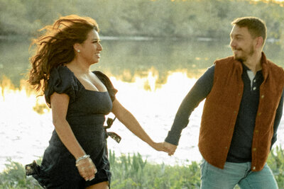 A fun, carefree moment of a couple running hand-in-hand by the lakeside in Houston, TX, during their engagement session
