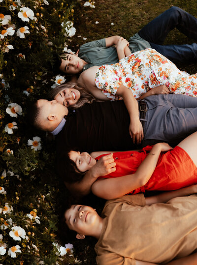 Family of five laying on the ground huddled together surrounded by wildflowers. 