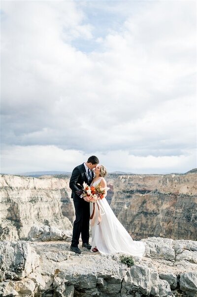 bride and groom kissing on rocky mountain cliff
