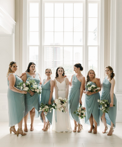 A bridal party surrounds their bride in front of the beautiful floor to ceiling windows in Flint's Durant Ballroom.