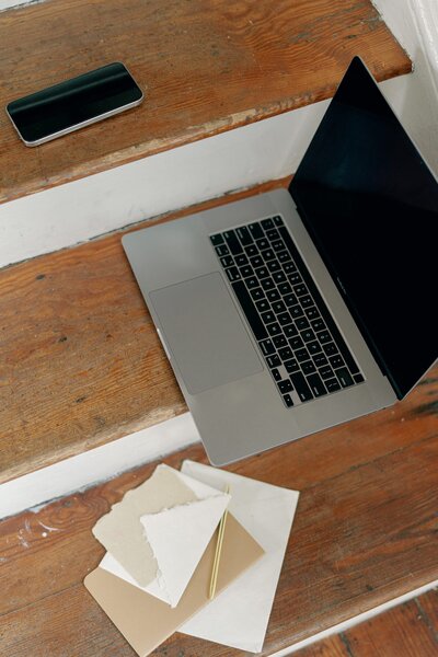 A laptop, phone, notebook, and papers on old wood stairs.