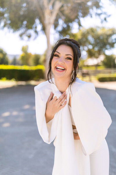 Girl with dark hair wearing flowy white blouse standing in street smiling