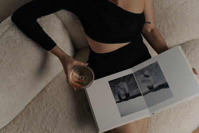 woman dressed in elegant black apparel sitting on white couch with mix drink in hand enjoying  her opened luxury wedding album on her lap - Romero Album Design