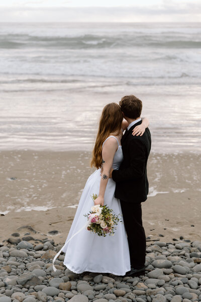Elopement couple embracing while standing on an Oregon Coast beach.