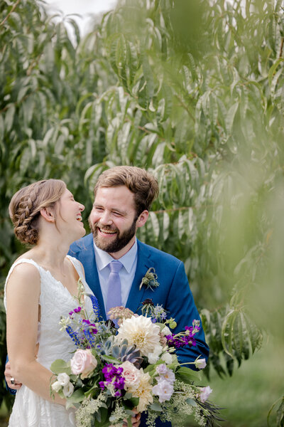 Bride and groom laugh together at an orchard wedding